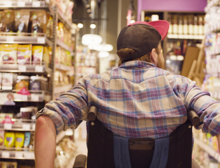 Une personne en fauteuil roulant se déplace dans les allées d'un supermarché 